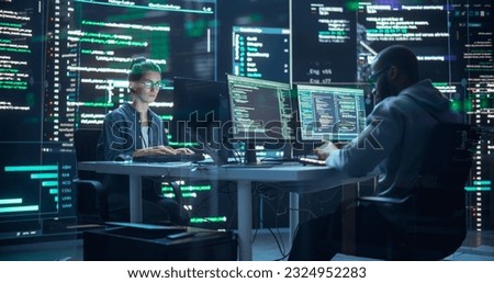 Portrait of Two Diverse Developers Working on Computer, Typing Lines of Code that Appear on Big Screens Surrounding Them. Male and Female Programmers Creating Innovative Software Together, Fixing Bugs Royalty-Free Stock Photo #2324952283