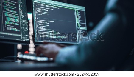 Close Up on Black Male Hands Typing on a Desktop Computer Keyboard In Dark Network Security Office. Professional Programmer Writing Code Displayed on Two Monitor Screens. High Tech Developing Concept.
