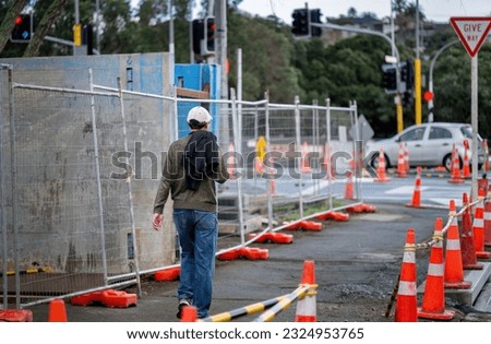 Man walking on sidewalk with orange traffic cones on one side and concrete blocks on the other side. Roadworks in Auckland. 