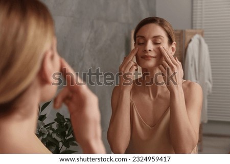 Woman massaging her face near mirror in bathroom Royalty-Free Stock Photo #2324959417