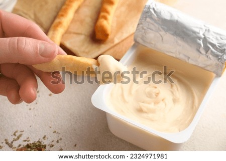 Woman eating tasty grissini with cream cheese on light background Royalty-Free Stock Photo #2324971981