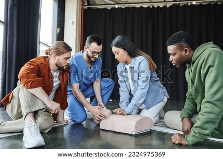 medical seminar, first aid training, cardiopulmonary resuscitation, healthcare worker assisting asian woman practicing chest compressions on CPR manikin near multicultural participants Royalty-Free Stock Photo #2324975369