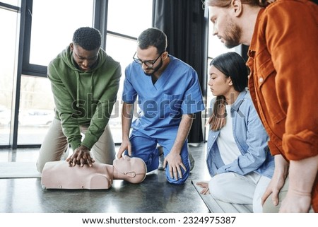 young multiethnic people and medical instructor looking at african american man doing chest compressions on CPR manikin, cardiopulmonary resuscitation, first aid training seminar