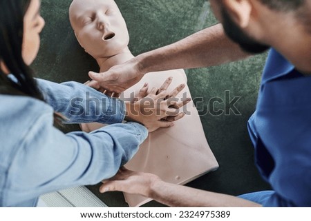 top view of young woman practicing chest compressions on CPR manikin during hands-on learning on first aid seminar near medical instructor, life-saving skills and techniques concept Royalty-Free Stock Photo #2324975389