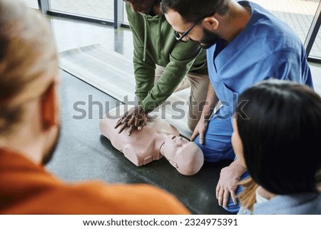 african american man practicing chest compressions and cardiopulmonary resuscitation on CPR manikin near medical instructor and young participants of first aid seminar in training room Royalty-Free Stock Photo #2324975391