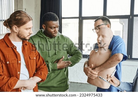 multiethnic participants of medical seminar looking at healthcare worker with CPR manikin showing first aid techniques in case of choking, emergency situations preparedness concept Royalty-Free Stock Photo #2324975433