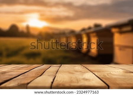 Empty wooden table top for product display. In the background, a blurred background of a small apiary at sunset.