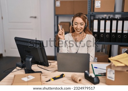 Hispanic woman working at small business ecommerce wearing headset smiling happy pointing with hand and finger to the side 