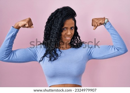 Middle age hispanic woman standing over pink background showing arms muscles smiling proud. fitness concept. 