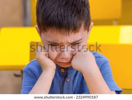 cute preschooler boy crying in classroom or outside with backpack in hands.dissatisfied unhappy sad upset angry kid child.back to school autumn time.yellow interior.tears on check. Royalty-Free Stock Photo #2324990187