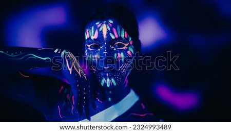 Young Dancer with Glowing Body Art Paint and White Clothes Creates Magic with Contemporary Dance Solo Routine. Choreographer Performs a Modern Dance Show on a Dark Stage Royalty-Free Stock Photo #2324993489