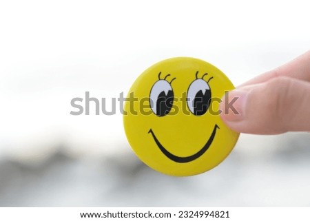 A hand holding a smiling face symbolizes a positive mindset, constructive feedback, a joyful approach to life, and a commitment to a healthy lifestyle.