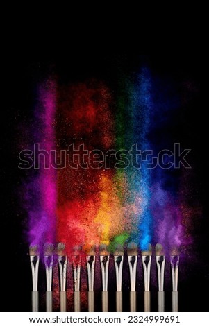 Explosion of multicolor shimmer powder dust, eye shadow, blush brushes on black background. Pigments for make-up. Abstract noisy texture background for cosmetic makeup concept.