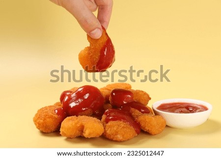 Woman holding delicious chicken nugget with ketchup on pale yellow background, closeup Royalty-Free Stock Photo #2325012447