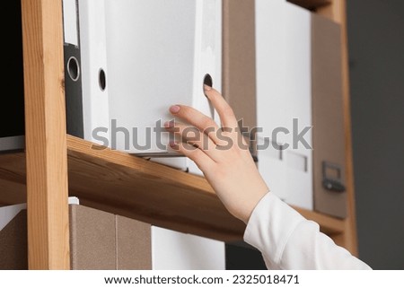 Woman taking folder with documents from shelf in office, closeup Royalty-Free Stock Photo #2325018471