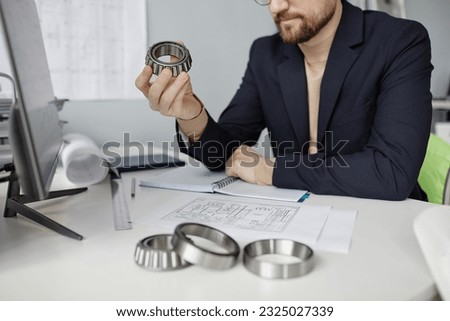 Closeup of mechanical engineer at workplace reviewing blueprints and holding machine part, copy space