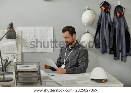 Minimal portrait of bearded male engineer working at desk in office against white wall with workwear in background, copy space Royalty-Free Stock Photo #2325027369
