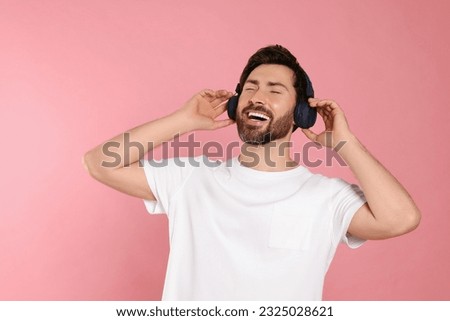 Happy man listening music with headphones on pink background