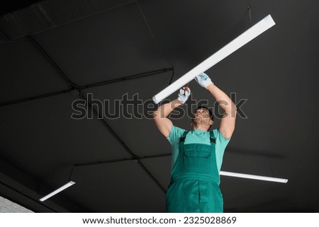 Ceiling light. Electrician installing led linear lamp indoors, low angle view. Space for text Royalty-Free Stock Photo #2325028869