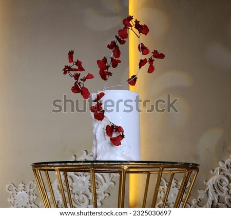 A white cake decorated with red flowers is placed on a glass table against a blurred background