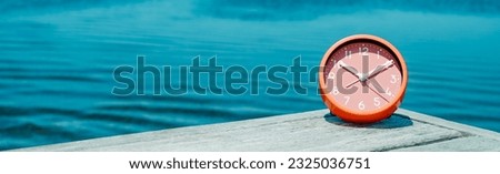 closeup of a pink clock on a wooden pier, next to the water, on a summer day, in a panoramic format to use as web banner or header