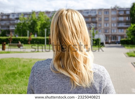 Lonely girl back view. Young woman with blond hair view from the back.Rear view of a young lady. Lonely blonde young woman is walking in the park.