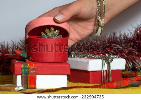 Pink paper Christmas box is being opened by a female hand, and contains Christmas decoration