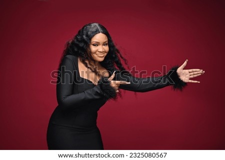 Photo of happy young and beautiful woman standing isolated over red wall background. She is looking to camera and showing copy space pointing. Product placement