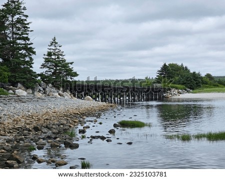 A side view of an old train bridge as it stretches over a rocky section of beach and extends across the water.