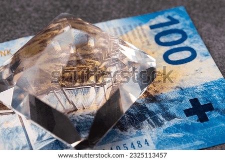 One hundred Swiss francs and a diamond. The banknote lies on a gray surface. Macro photo with lots of small details.
