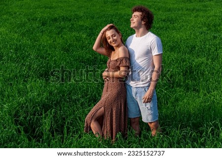 A guy and a girl are hugging on a green field. Romantic photo session of a couple in love on a green wheat field