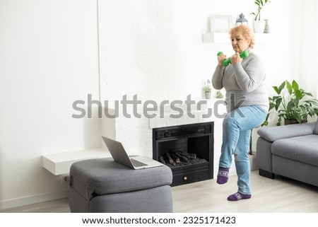 Sport In Mature Age. Happy senior woman doing stretching exercises in front of laptop at home, watching online tutorials, free space.