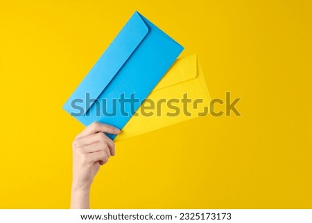 Female hand holding blue and yellow envelopes on yellow background
