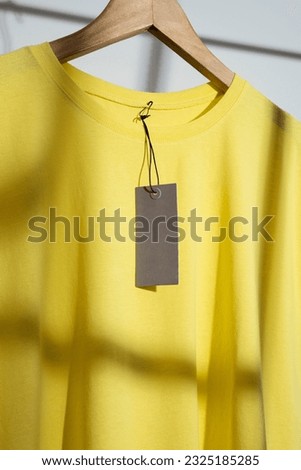 Yellow t-shirt with blank price tag mockup, template on wooden hanger. 