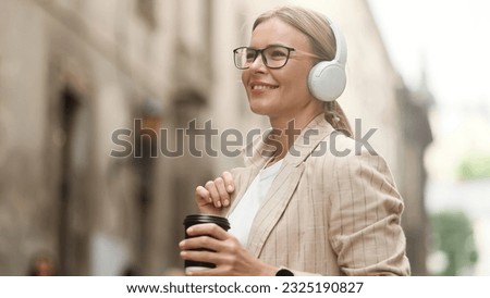 Serene calm mature blond woman with headphones hold cup with hot coffee or tea at urban city street Relaxed middle aged female enjoying great day and listening to music outdoors Beautiful day concept Royalty-Free Stock Photo #2325190827