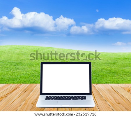 Laptop computer on wooden floor with green fields and blue sky background