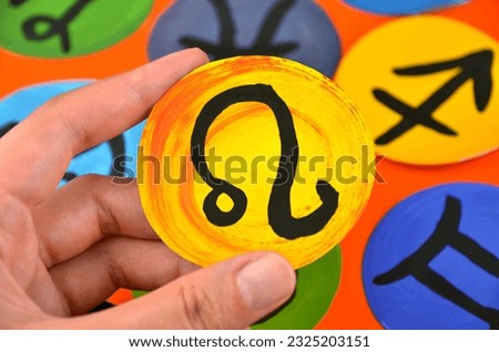 Different round astrology (zodiac) signs on an orange background + yellow leo sign closeup in a hand