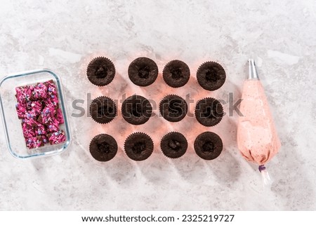 Flat lay. Piping strawberry buttercream frosting on top of chocolate cupcakes.