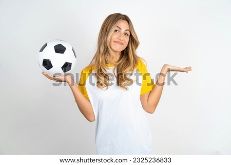 Careless attractive Young beautiful woman holding football ball over white background  shrugging shoulders, oops. Royalty-Free Stock Photo #2325236833