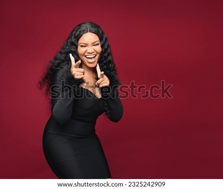 Beautiful African woman so happy and confident showing a big smile surprised finger, indoors on red isolatable background Royalty-Free Stock Photo #2325242909