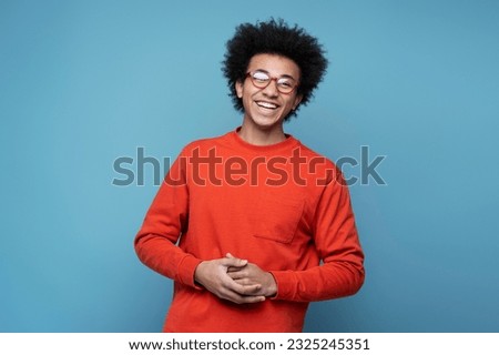 Happy smiling African American man with curly hair wearing stylish casual clothing isolated on blue background. Cheerful successful student in eyeglasses looking at camera. Education concept 