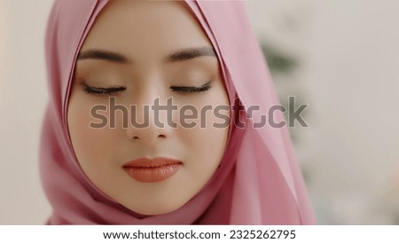 Closeup head shot of a beautiful Asian Muslim woman covering her beauty with head scarf and closing her eyes.