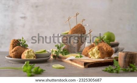 Cod dumplings, or "bolinhos de bacalhau" and parsley leaves and lemons on wooden cutting board in a kitchen counter top.