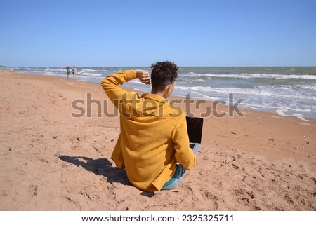 Young attractive student on vacation. The guy is working on a laptop by the sea.