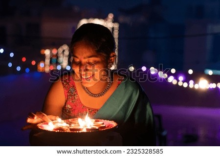 Beautiful Indian woman placing diya with smiling at home on Diwali Royalty-Free Stock Photo #2325328585