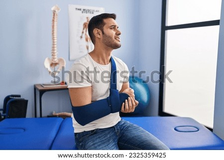 Young hispanic man injured physiotherapy patient suffering for arm pain at rehab clinic Royalty-Free Stock Photo #2325359425
