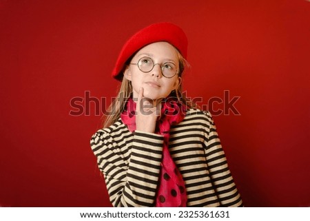 Portrait of a girl in a red beret, red bow and striped blouse. Red background. place for text