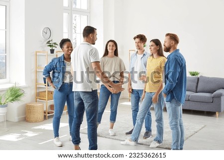 Group of diverse friends having a discussion. Several young multiracial people standing in the living room at home and listening to a young man talking about something Royalty-Free Stock Photo #2325362615