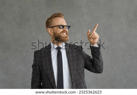Portrait of a successful cool businessman in funny pixel glasses on a gray background. Creative man in suit confidently points finger looking to the side. Concept of successful business investment.