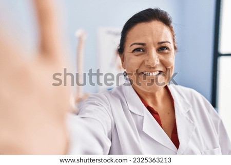 Middle age hispanic woman physiotherapist making selfie by the camera at rehab clinic